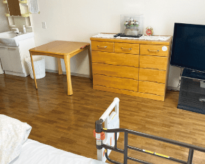 木製家具が配置された居室。テーブルとチェスト、テレビが見える。